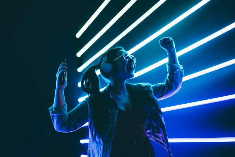 Woman in headphones listening music and dancing in neon light.